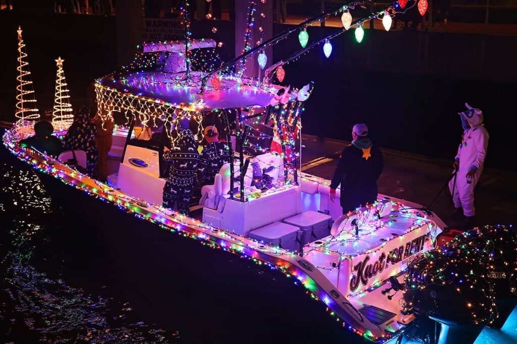 Fishing boat decked in multicolored Christmas lights with a crew dressed in pjs and onsies