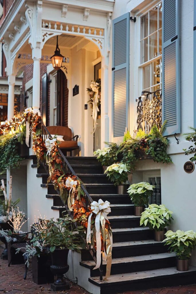 Elegant white home with blue shutters decorated for Christmas in Savannah with Magnolia-leaf garlands and white poinsettias on the staircase