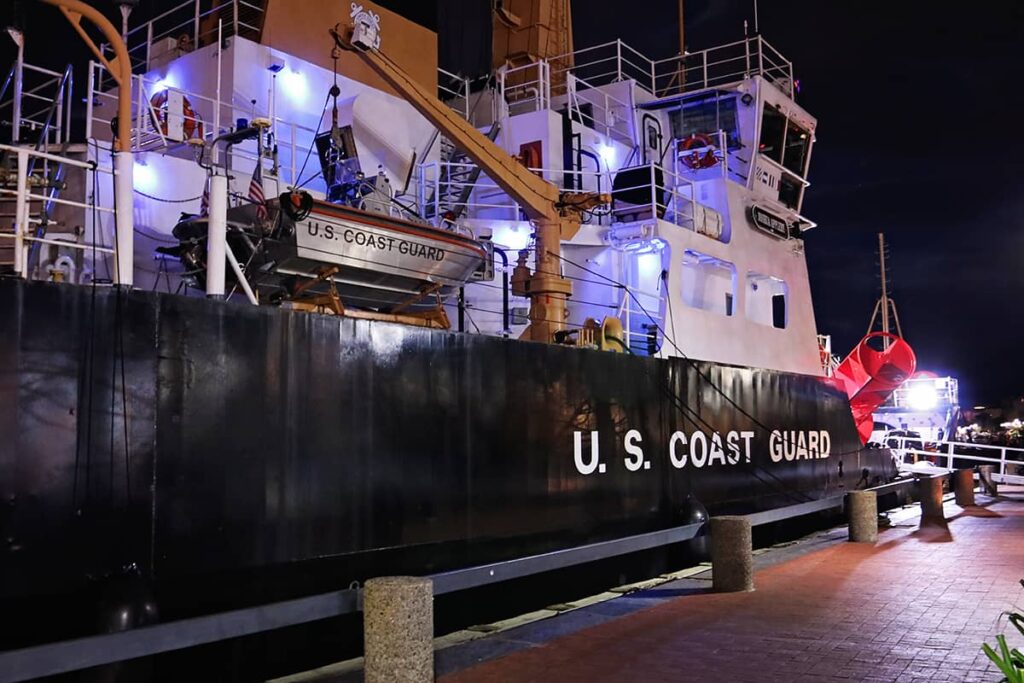 Side view of a U.S. Coast Guard Ship docked on River Street in Savannah, Georgia at night with purple lights illuminating the deck