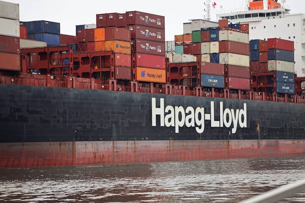 A blue and red cargo ship loaded down with containers and the words "Hapag-Lloyd" in white on the side
