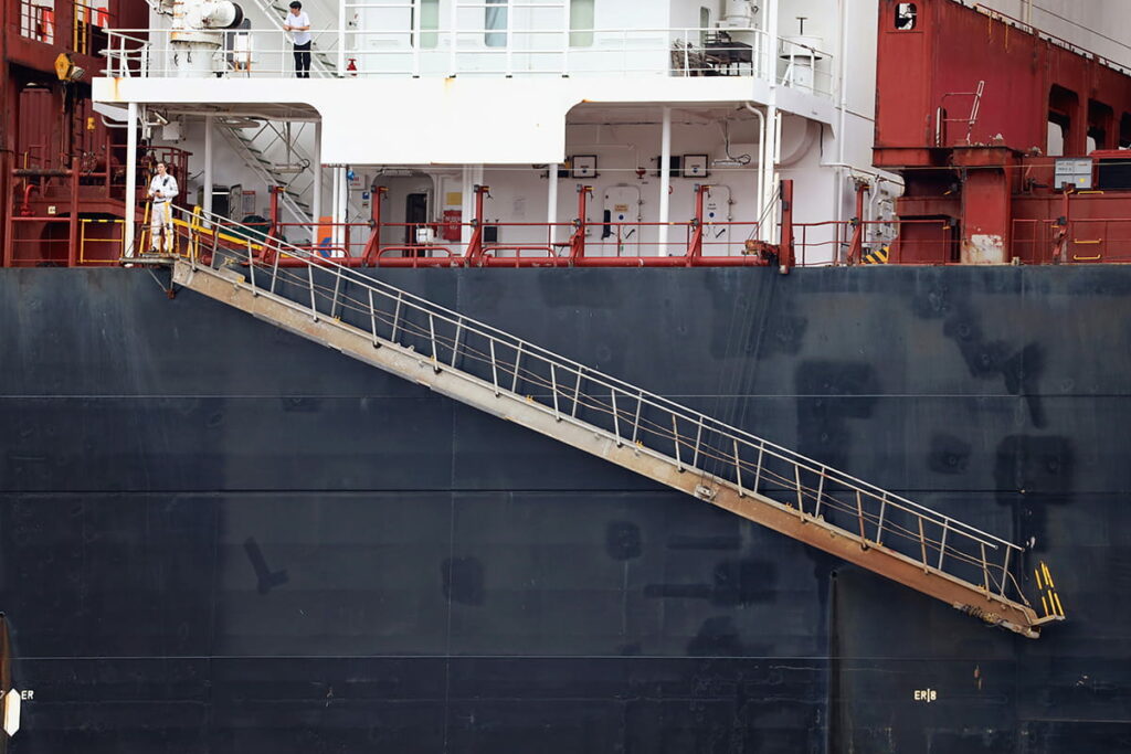 The navy-blue hull of a cargo ship in Savannah with metal steps attached at an angle