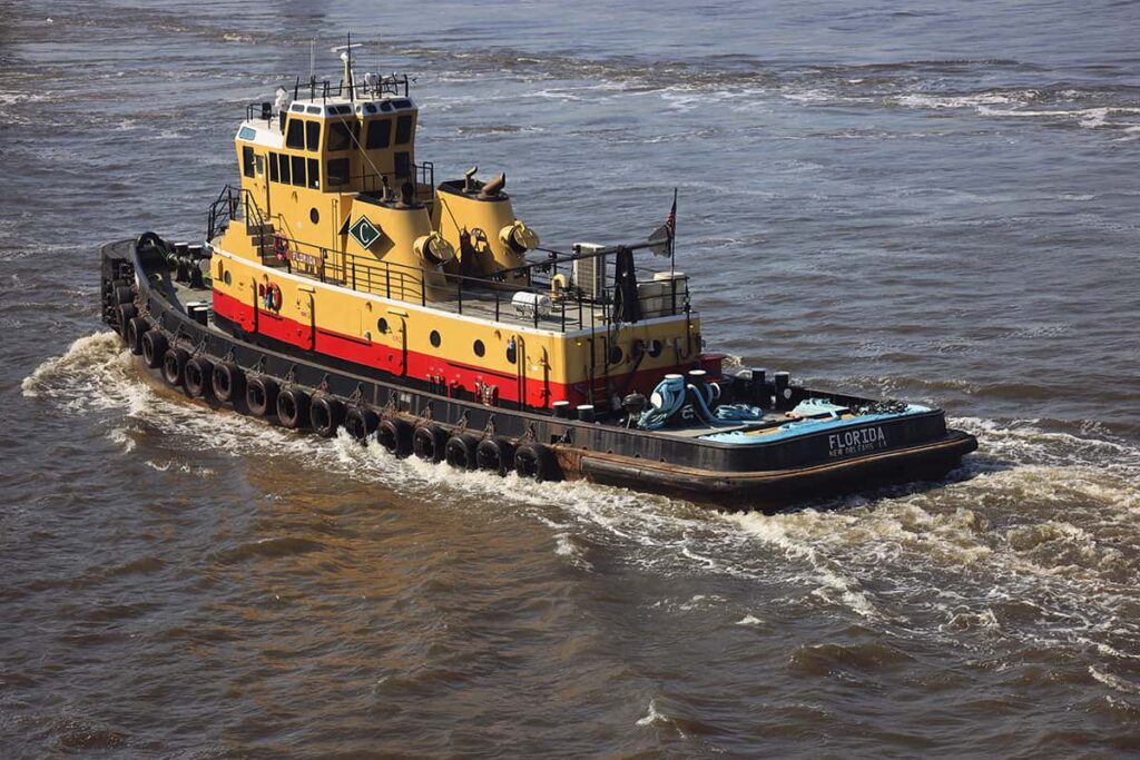 Aerial view of the Florida tugboat as it heads upriver in Savannah. It's yellow and red above the deck and has a black hull