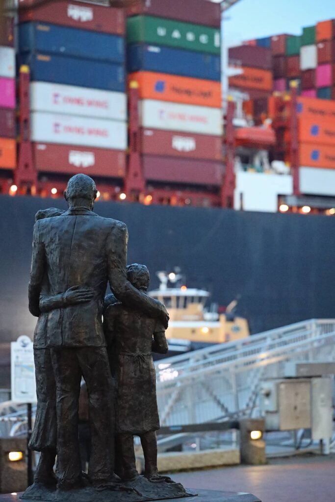 The African American Monument on River Street in Savannah shows a family of four looking towards the river as a giant cargo ship passes by, loaded with colorful shipping containers