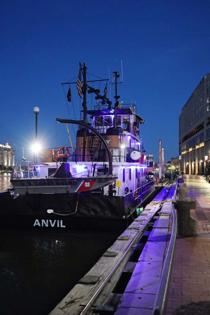 White lettering spelling "ANVIL" pops against a dark background on the stern of a U.S. Coast Guard ship docked along River Street in Savannah. Purple lights illuminate the deck of the vessel