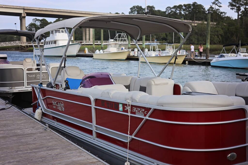 Red pontoon with a tan cover docked at Palmetto Bay Marina on Hilton Head Island. Small craft with yellow hulls and blue hulls are docked in the background