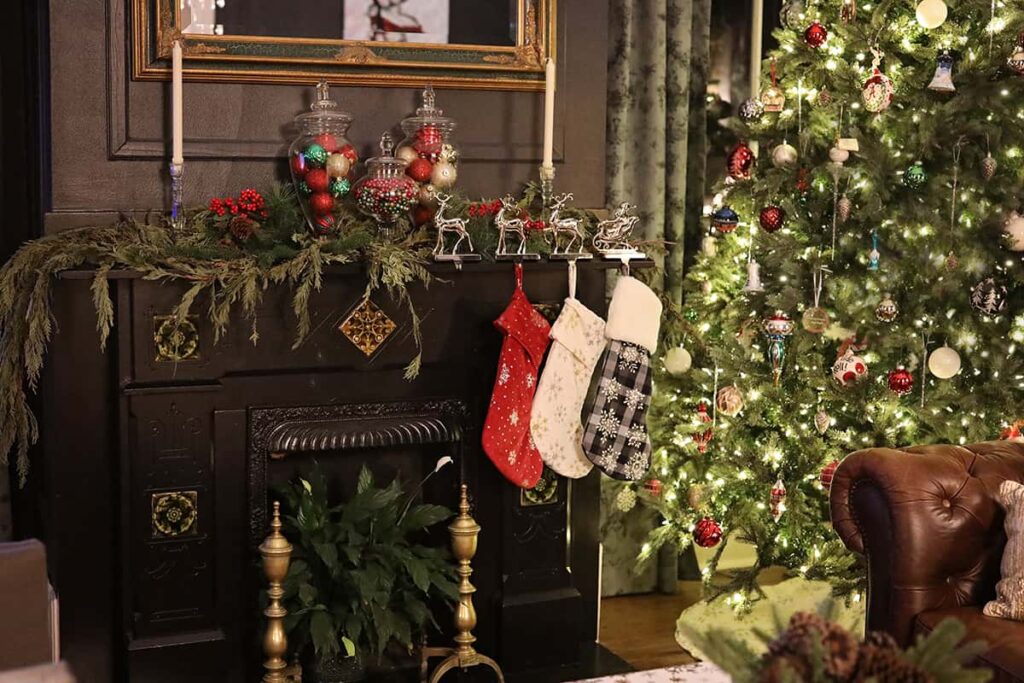 Masculine looking study at the Thomas Weihs Haus. The fireplace surround is painted a dark charcoal and the curtains have a dark pattern. A Christmas tree is beside the fireplace and stockings hang from the mantle