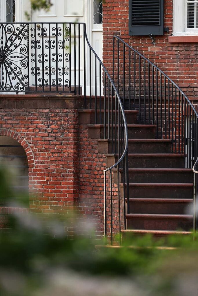Close-up of the curved staircase to the right of the entrance of the Davenport House Museum. The railings at the top of the staircase are made from wrought iron with a large floral design and lots of smaller filigree shapes