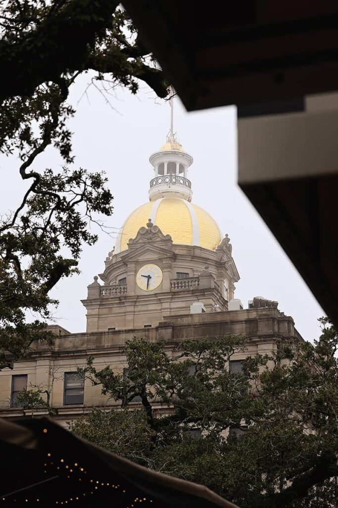Peering through tree branches towards the gold dome of Savannah's City Hall enveloped in fog