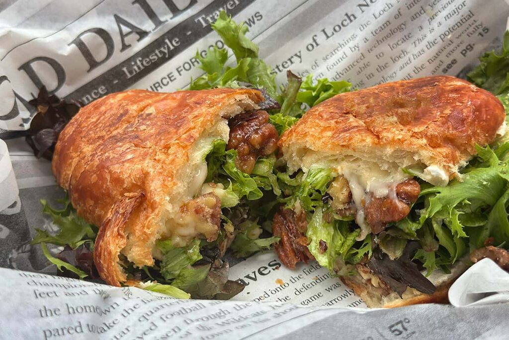 The brie and walnut sandwich from Urban Deli, served on a croissant. It includes melted brie, candied walnuts, drizzled honey, spring lettuce mix, and olive oil