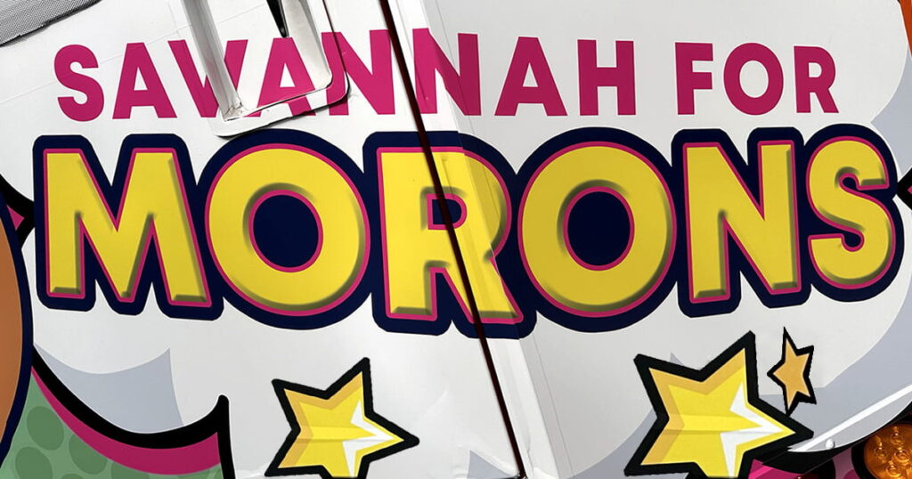 Close-up of the Savannah for Morons logo on the back of a trolley. The lettering is in pink, black, and yellow, and there are yellow stars beneath the logo